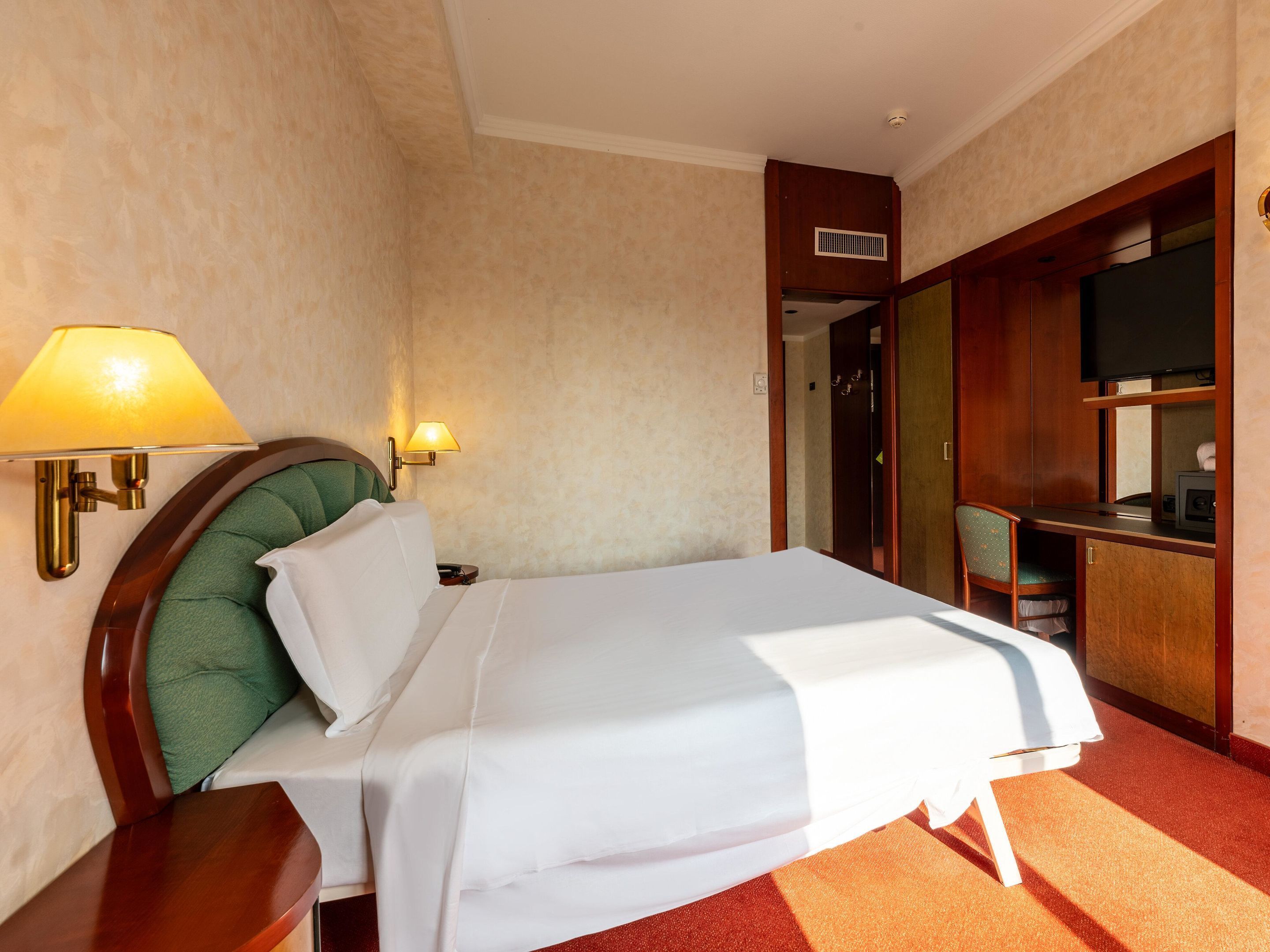 Una habitación de hotel con cama, mesita de noche, lámpara, televisor y armario.