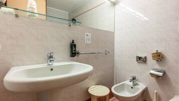 A bathroom with a sink, bidet, and a glass shelf above the mirror.