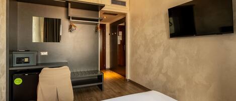 Habitación de hotel con cama, escritorio con computadora, televisor montado en la pared y perchero.