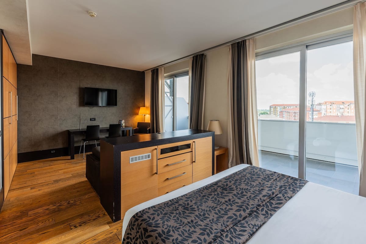 A hotel room with a bed, a desk, a chair, a TV, and a view of the city.