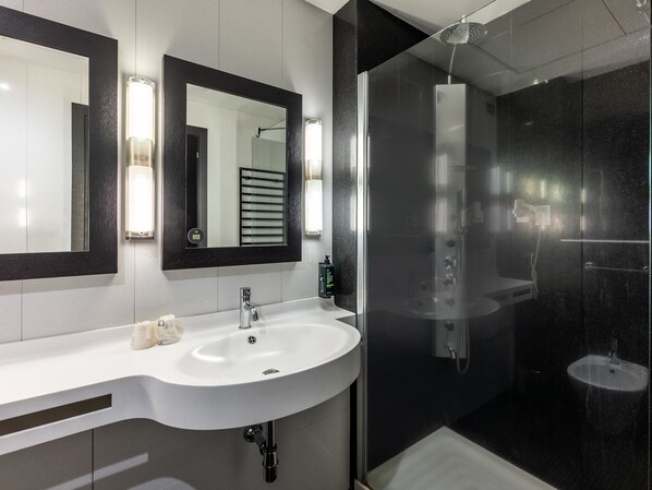 A modern bathroom with a white sink, two mirrors, a glass shower enclosure, and a handheld showerhead. - B&B Hotel Borgaro Torinese (Borgaro Torinese)