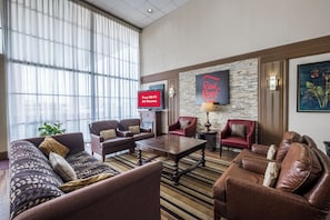 A hotel lobby with leather sofas, a coffee table, a TV displaying 'Free Wi-Fi All Rooms,' and a 'Red Roof Inn' sign. - Red Roof Inn Meridian (Meridian)