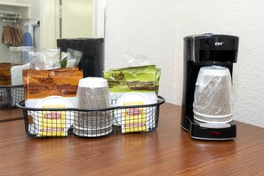 Una cafetera y una cesta con bolsitas de té Lipton y un infusor sobre una mesa de madera.