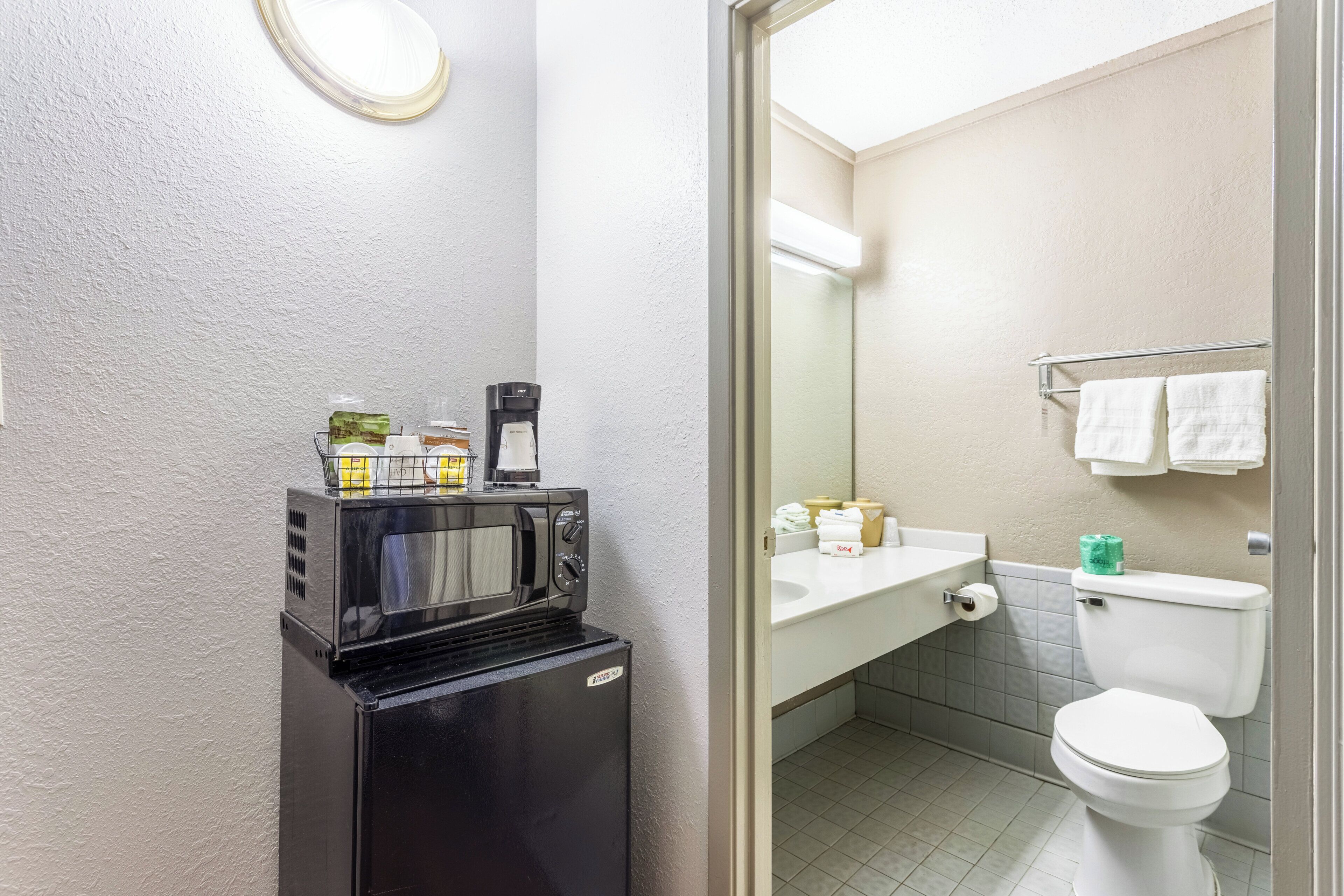 A compact bathroom with a black coffee machine, a white sink, and a toilet.