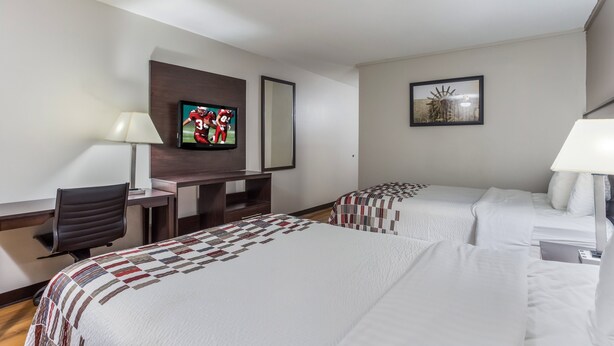 A hotel room with two beds, a desk, a TV, and a lamp. - Red Roof Inn Meridian (Meridian)