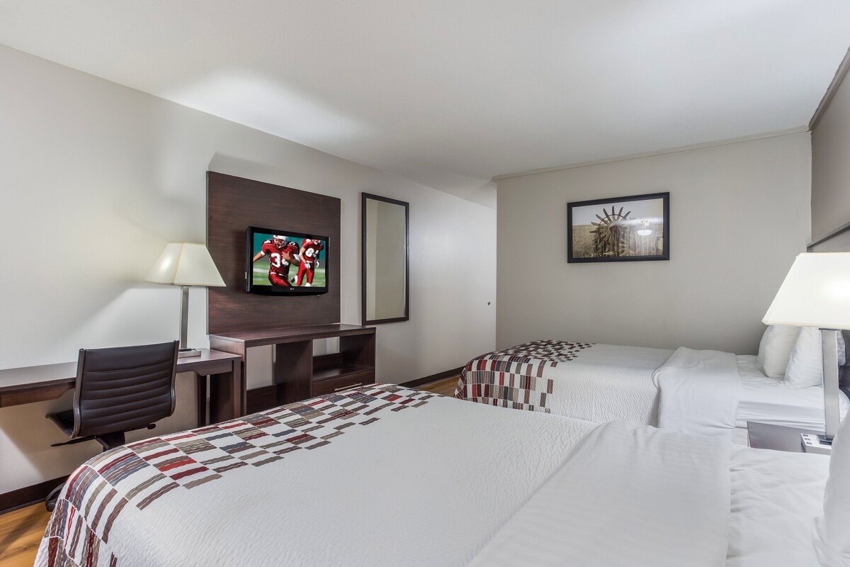 Habitación de hotel con dos camas, un escritorio, un televisor y una lámpara.