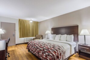 A hotel room with a bed, two bedside lamps, a chair, a desk, and a window with curtains. - Red Roof Inn Meridian (Meridian)