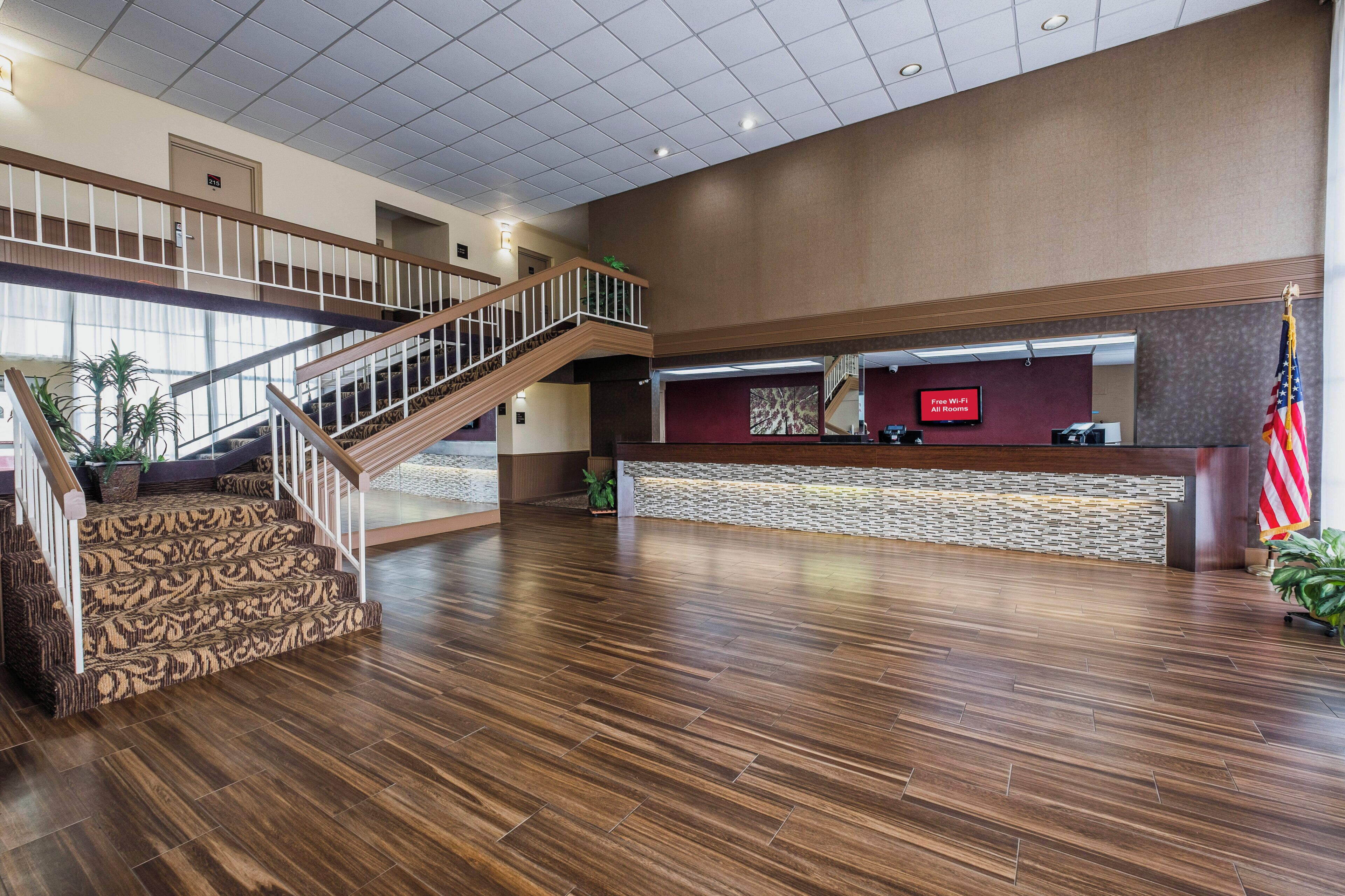 A spacious lobby with a wooden staircase, a reception desk, and an American flag.