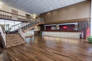 Un hall d’entrée spacieux avec un escalier en bois, un comptoir d’accueil et un drapeau américain.