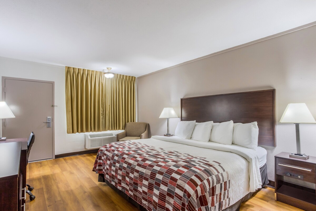 Habitación de hotel con cama, dos mesitas de noche con lámparas, una silla, un escritorio y una ventana con cortinas.