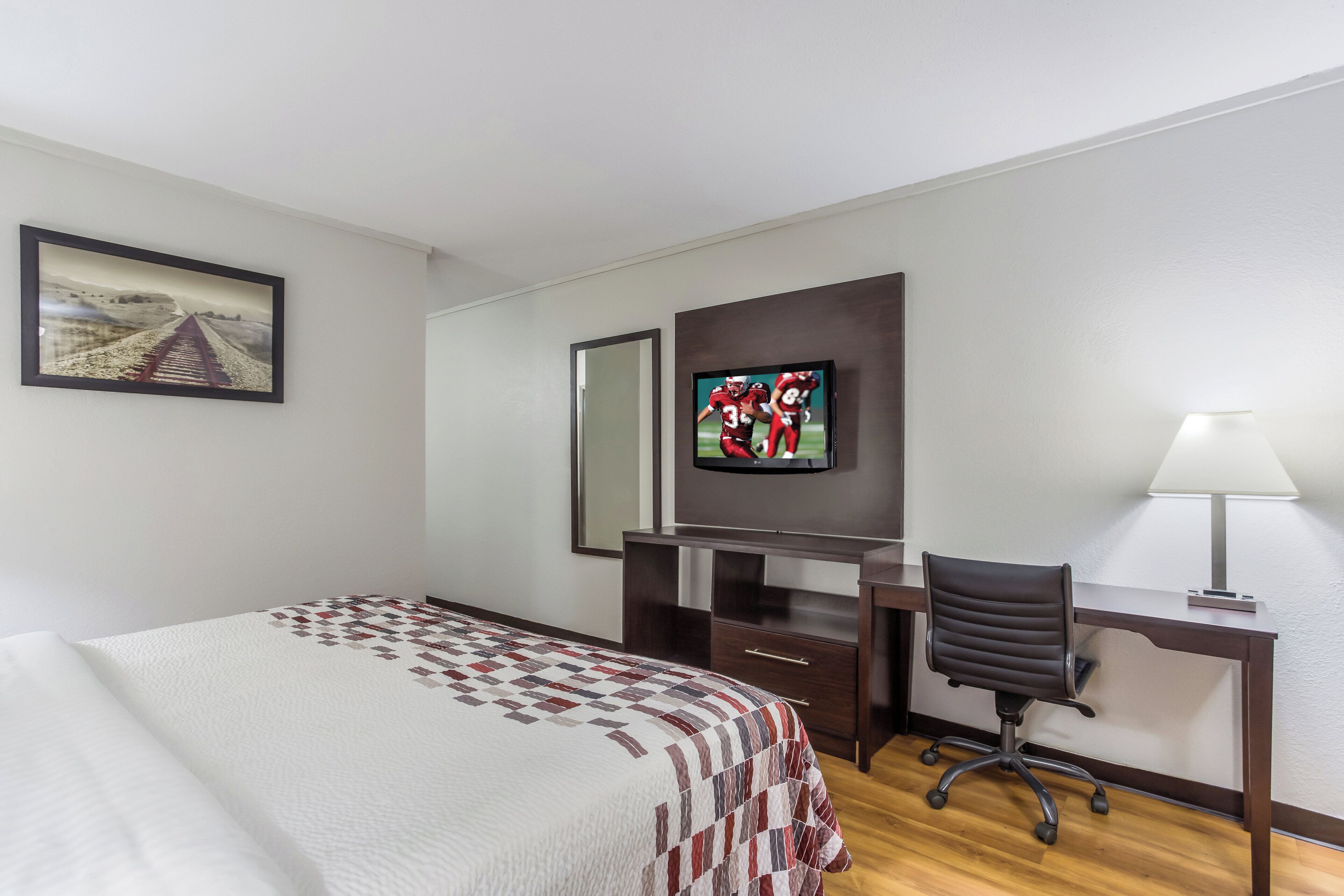 A hotel room with a bed, a desk with a chair, a television, and a lamp.
