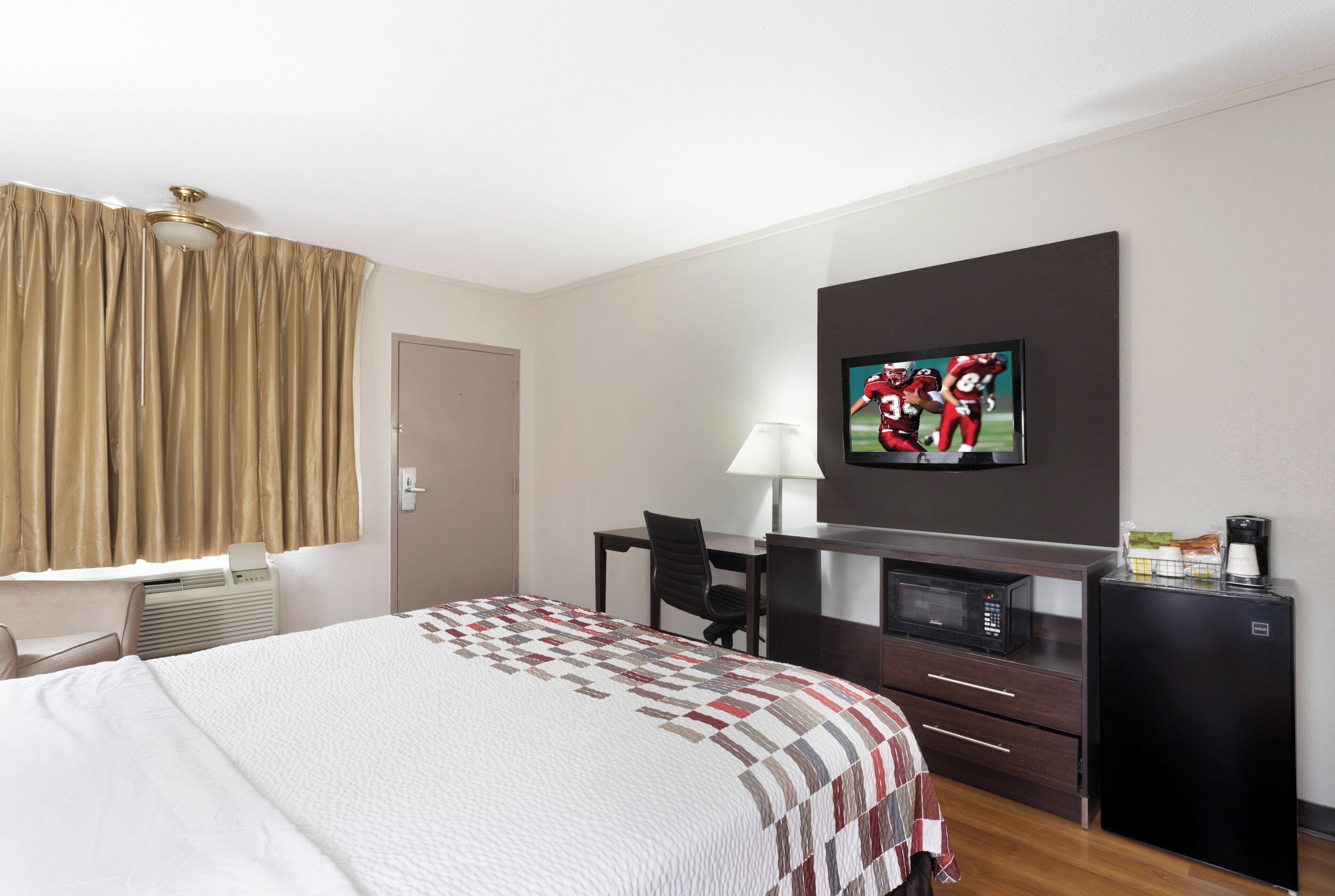 A hotel room with a bed, a desk, a television, a lamp, a coffee maker, and a microwave.