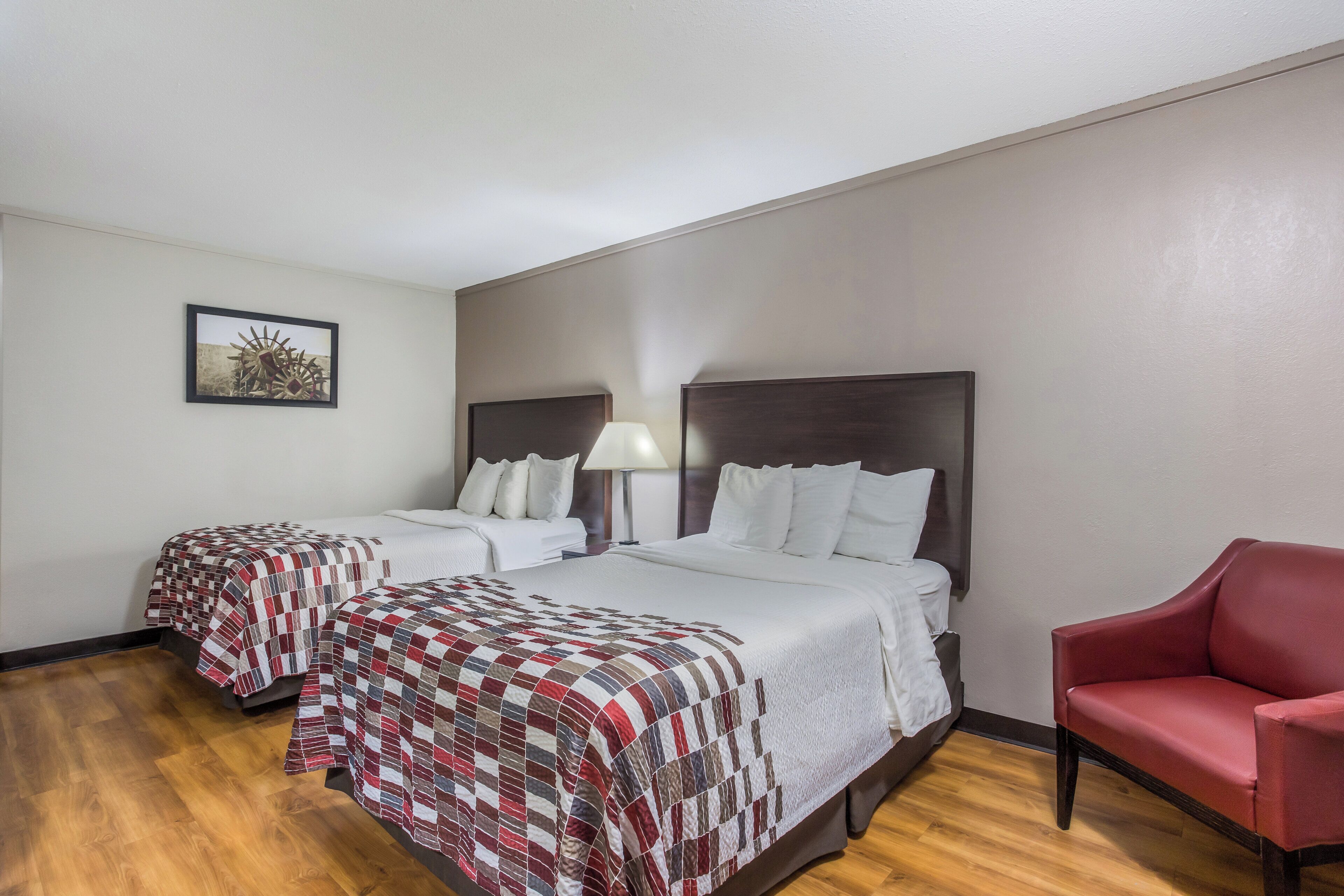 A hotel room with two beds, a red armchair, and a single bed with a quilt.