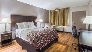 A hotel room with a bed, bedside tables, a desk, a chair, a desk lamp, a ceiling fan, and a window with curtains. - Red Roof Inn Meridian (Meridian)