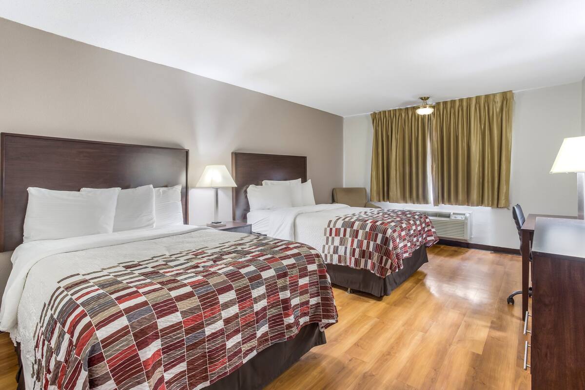 A hotel room with two beds, a desk, and a window with curtains.