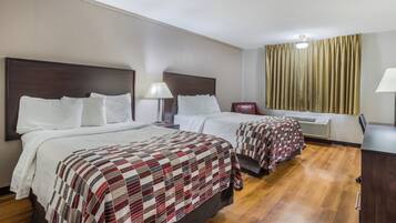 A hotel room with two beds, a wooden floor, a window with curtains, and a ceiling light.
