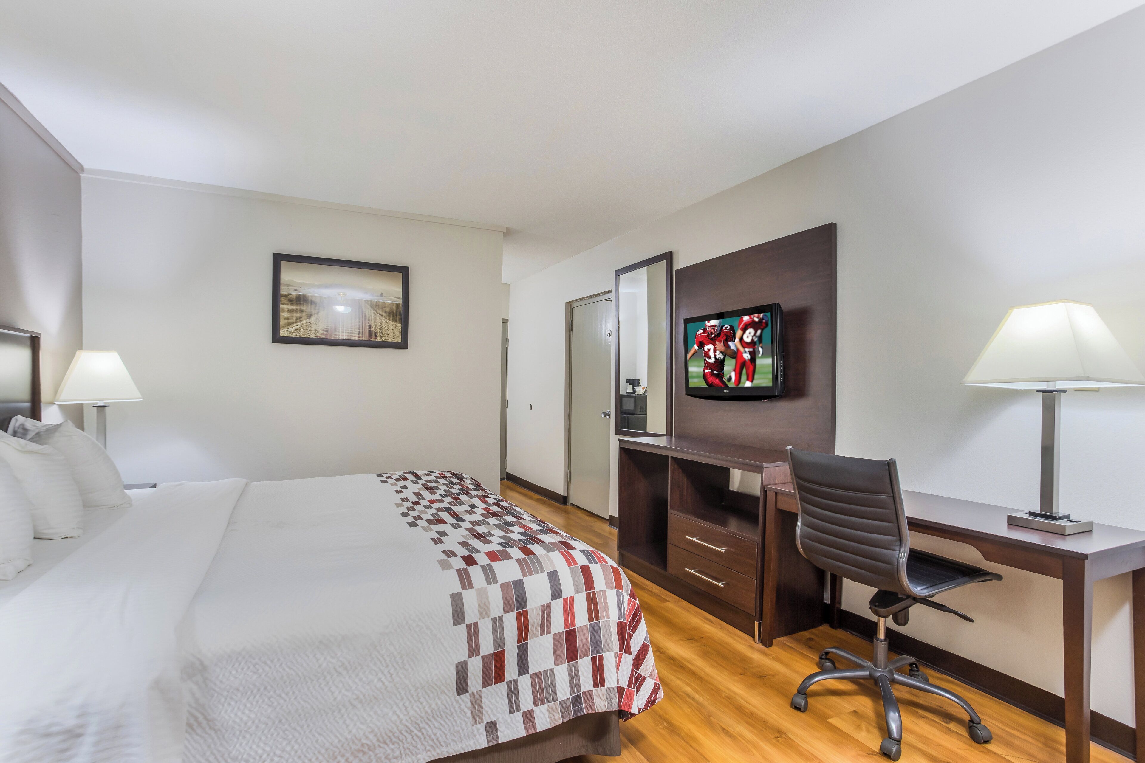 Een hotelkamer met een bed, een bureau, een stoel, een televisie en een lamp.