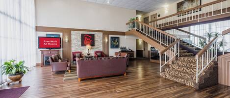 A spacious hotel lobby with a large sofa, a fireplace, a staircase, and a sign indicating free Wi-Fi.