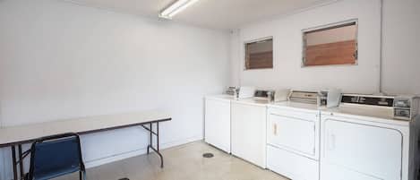 Uma lavanderia com mesa, cadeiras e várias máquinas de lavar roupa.