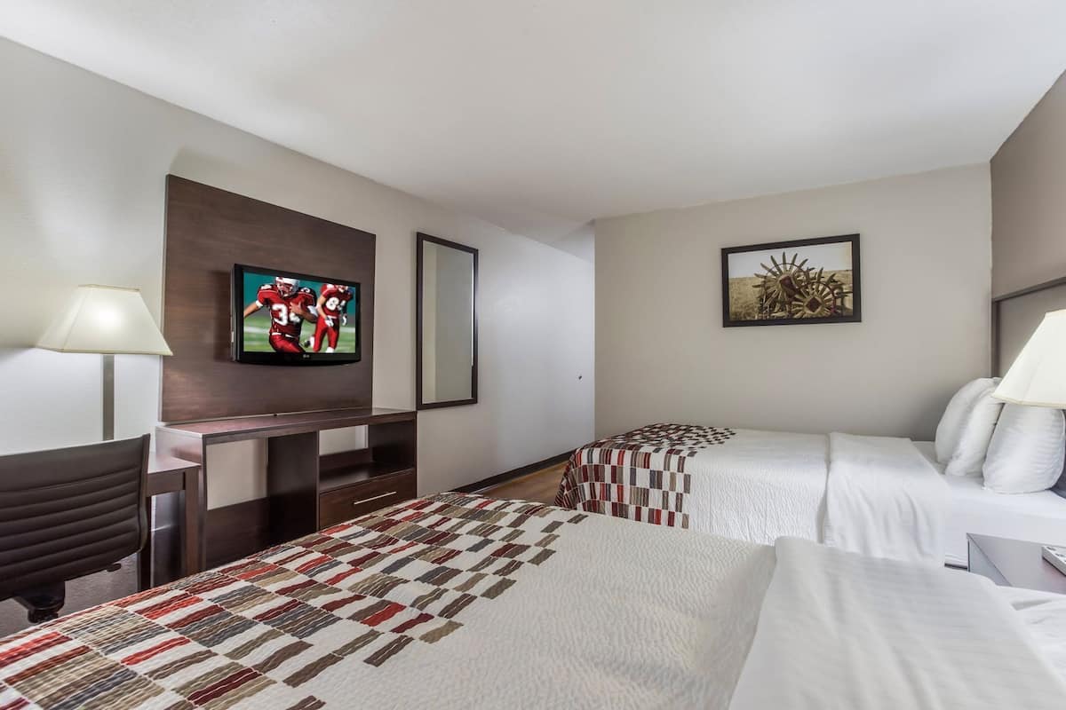 A hotel room with a TV, two beds, a desk, and a lamp.