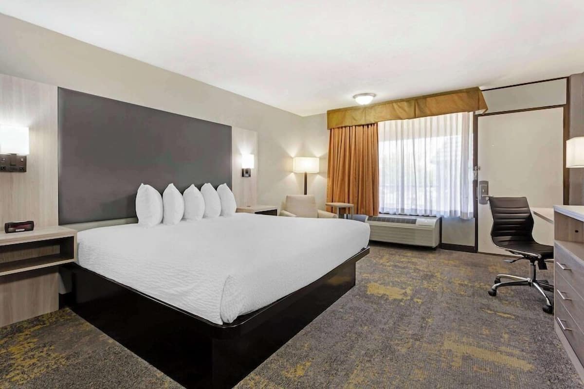 A hotel room with a large bed, a desk, a chair, a lamp, and a window with curtains.