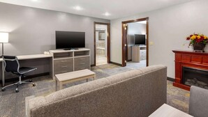 A hotel room with a flat-screen TV, a desk with drawers, a comfortable sofa, a small table, and a fireplace. - Best Western Plus Weston Inn (Logan)