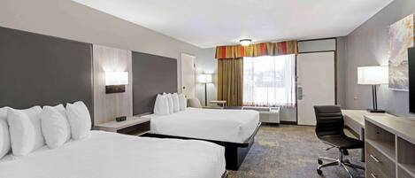 A hotel room with two beds, a desk, a chair, and a television.