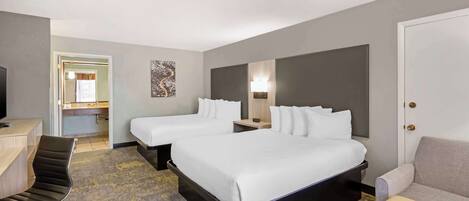 A hotel room with two beds, a desk, a chair, and a sofa.