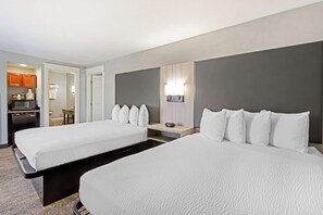 A hotel room with two beds, a desk, a lamp, and a kitchenette.