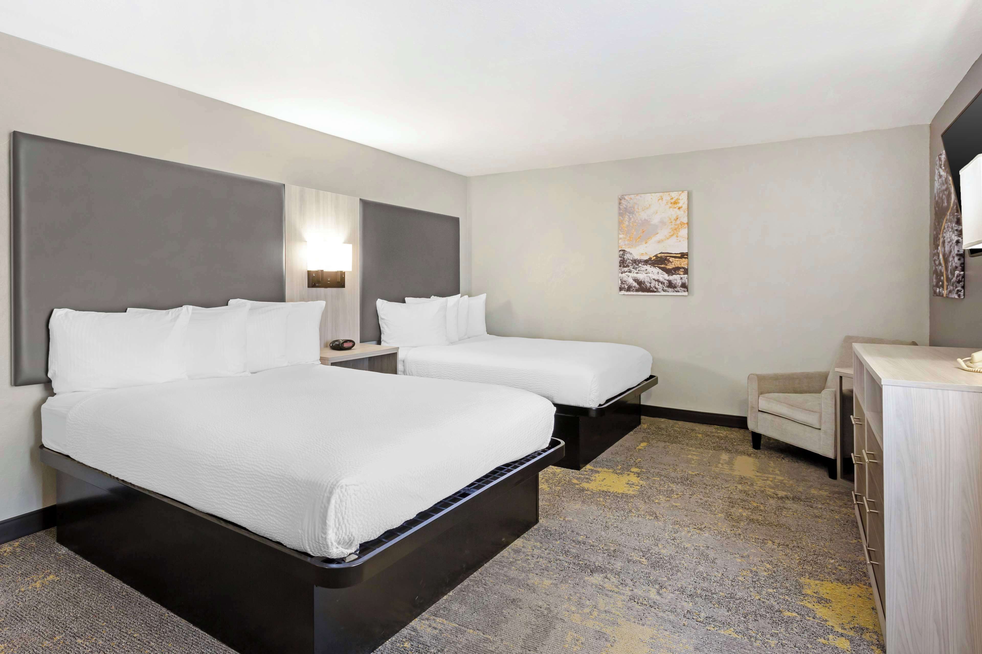 A hotel room with two beds, a desk, a chair, and a painting on the wall.