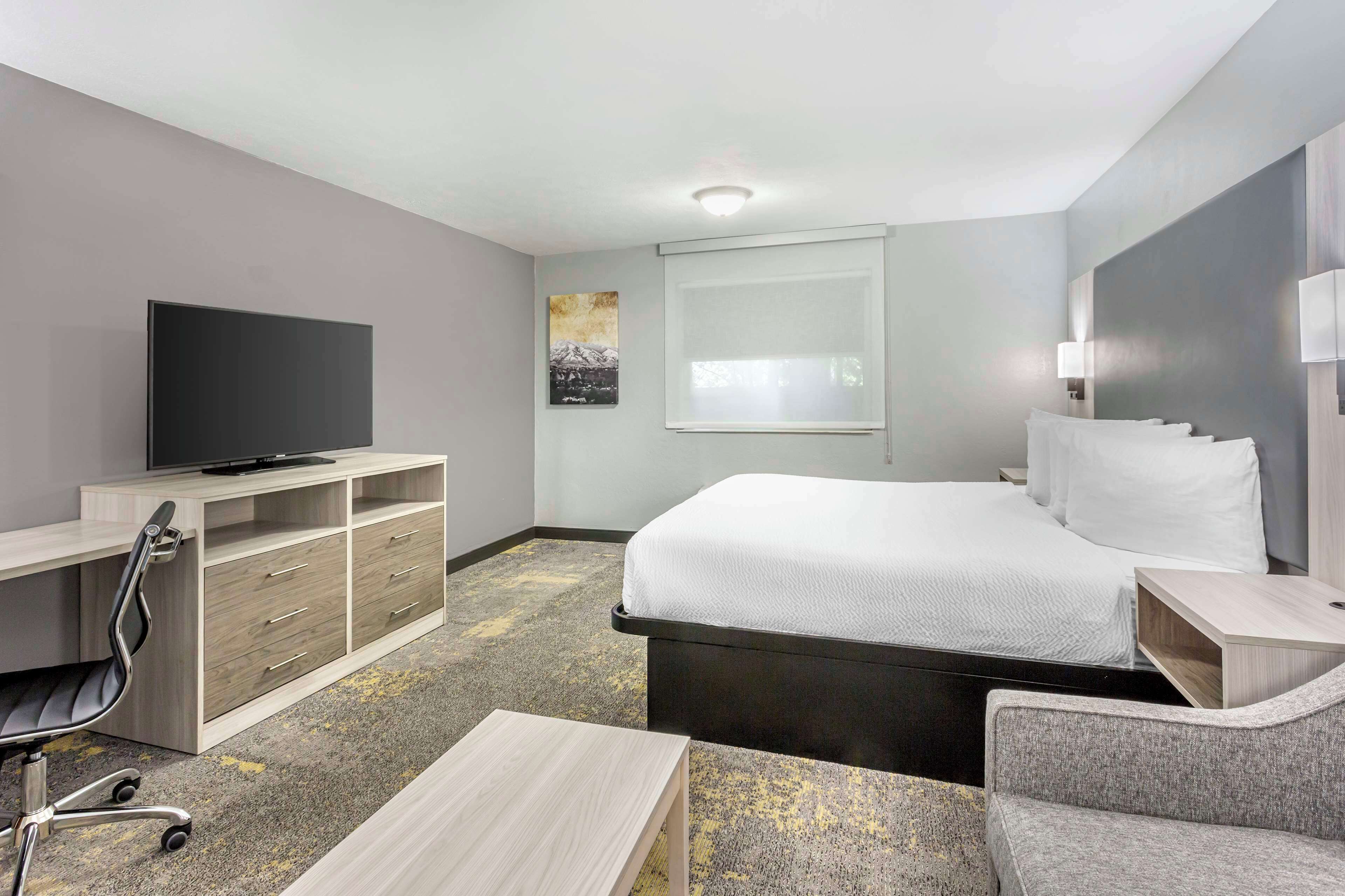 Une chambre d’hôtel comprenant un lit, un bureau avec une chaise, une télévision et une fenêtre avec des stores.