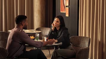 A couple seated at a round table in a room with patterned furniture and curtains.