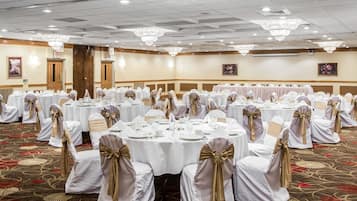 Un salón de banquetes con mesas redondas, manteles blancos y sillas con cintas doradas.