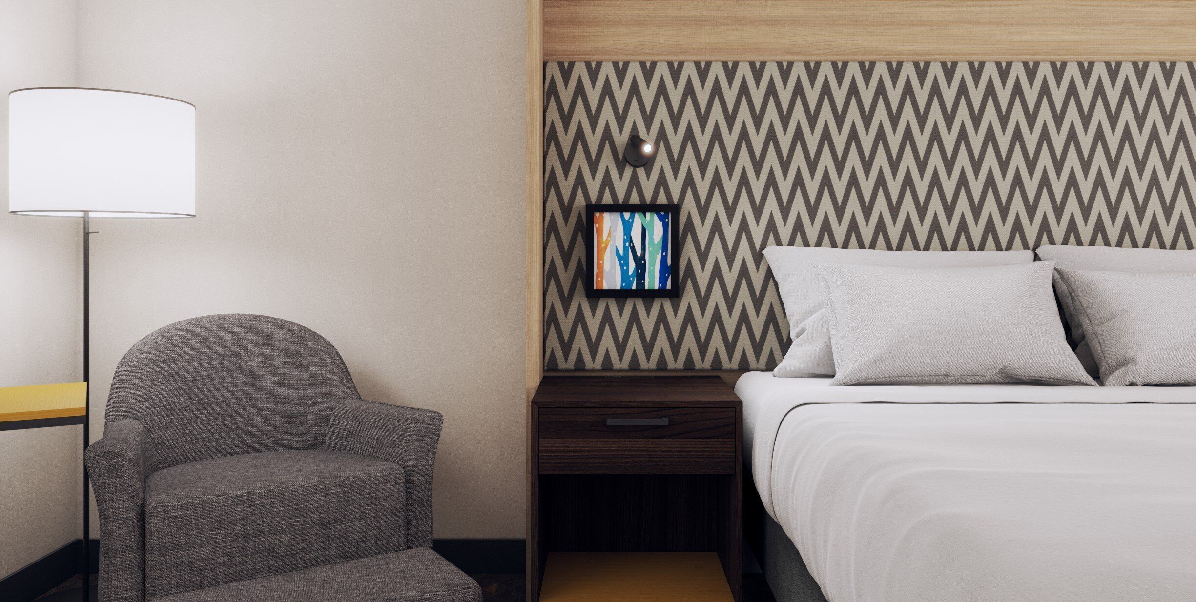 A hotel room with a bed, a chair, a bedside table, a lamp, and a wall-mounted picture.