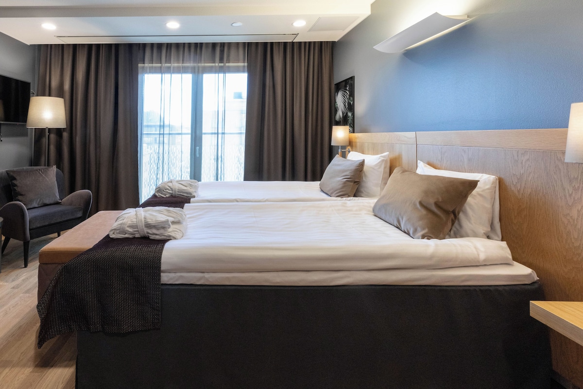 A hotel room with a large bed, a desk, a chair, and a window with curtains.