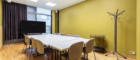 A conference room with a white table, chairs, a projector screen, and a coat stand.