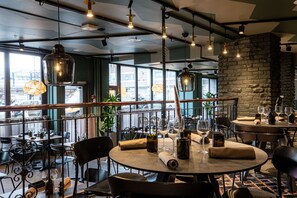 A restaurant with round tables, black chairs, hanging light fixtures, and a view of the city through large windows. - Scandic Tampere City (Tampere)
