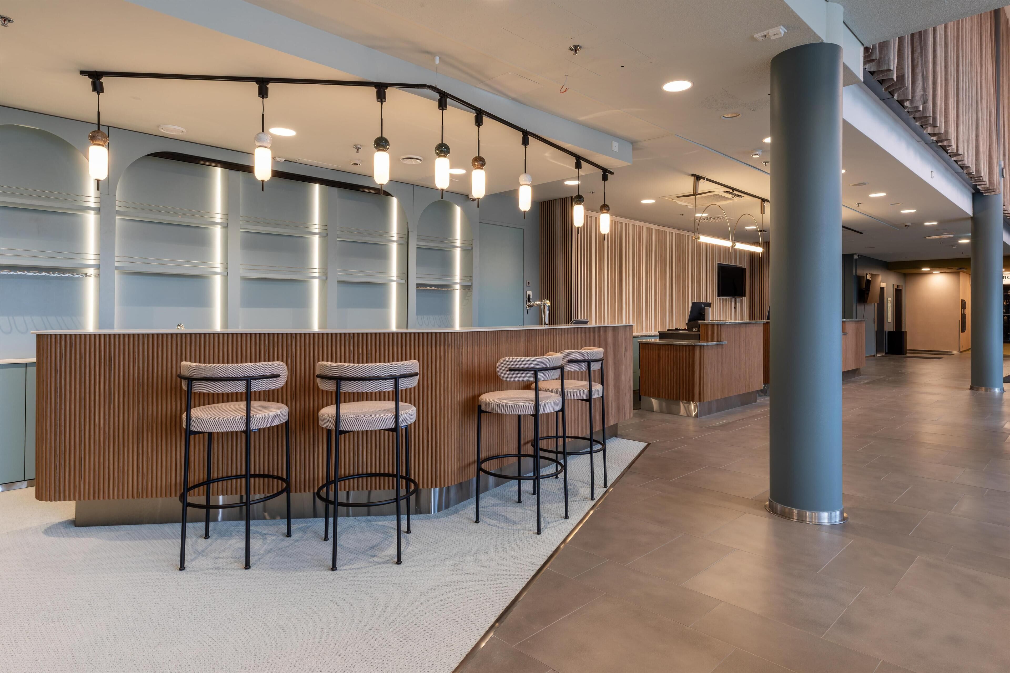 Un espace d’accueil moderne avec un comptoir incurvé, des tabourets de bar et des luminaires suspendus.