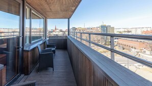 A balcony with wooden flooring and wicker furniture, overlooking a cityscape with buildings and a tower. - Scandic Tampere City (Tampere)