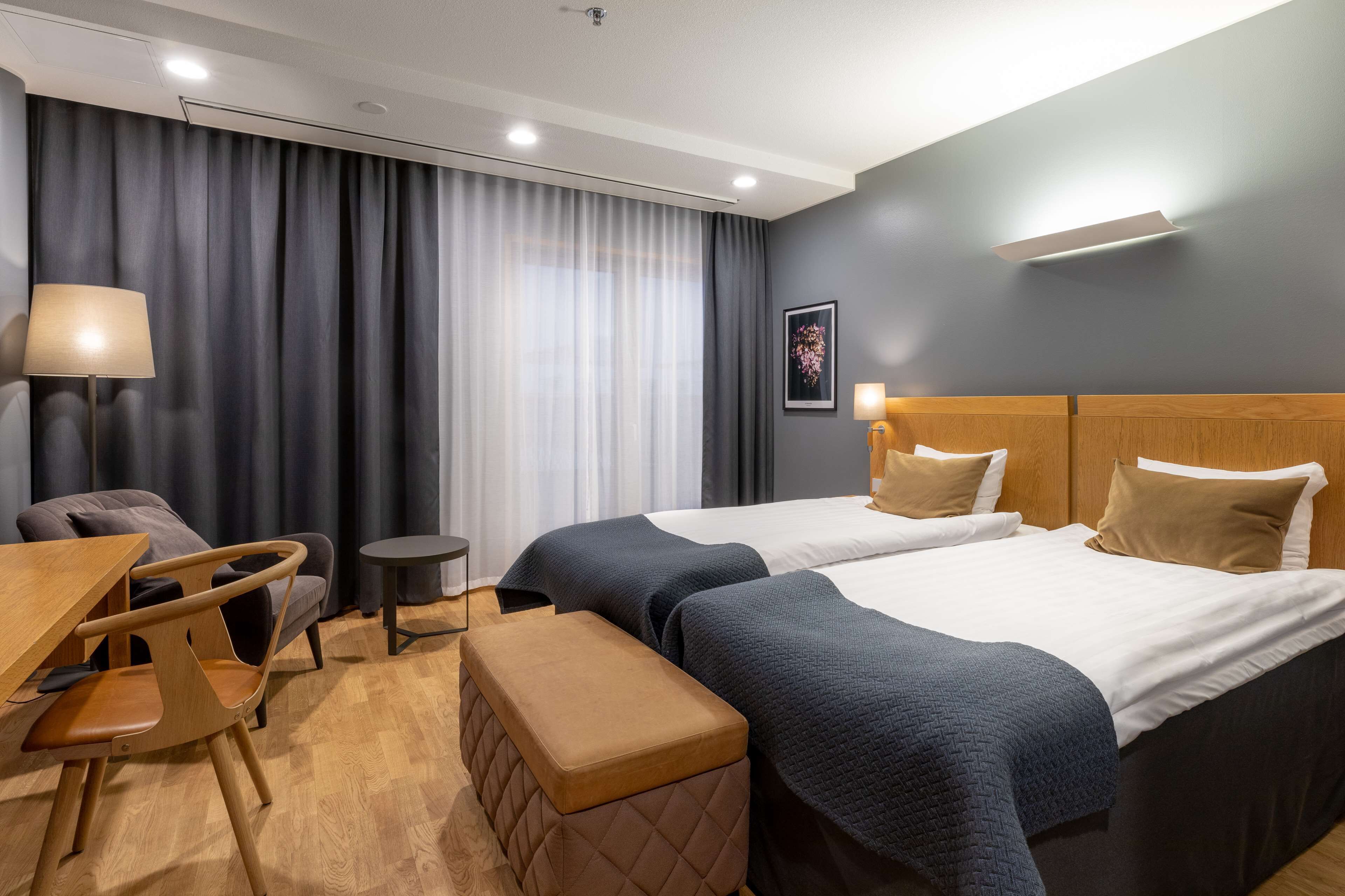 Une chambre d’hôtel avec deux lits, un bureau, une chaise, une petite table et un banc.