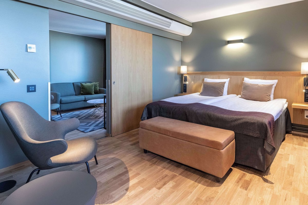 Ein modernes Hotelzimmer mit Bett, Sofa, Sessel und Bank.
