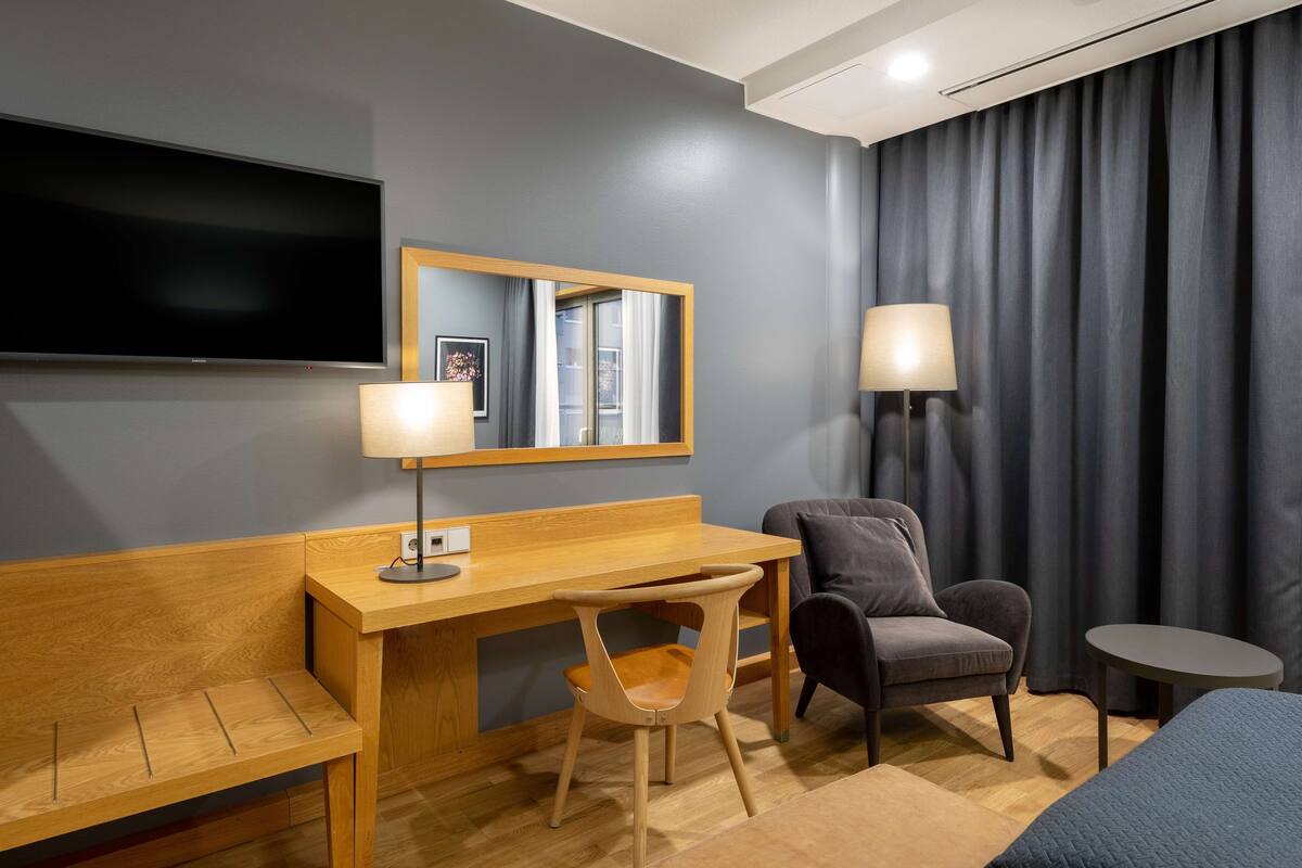 Ein Hotelzimmer mit einem Holztisch, zwei Stühlen, einem Fernseher, einer Lampe und einem Bett.