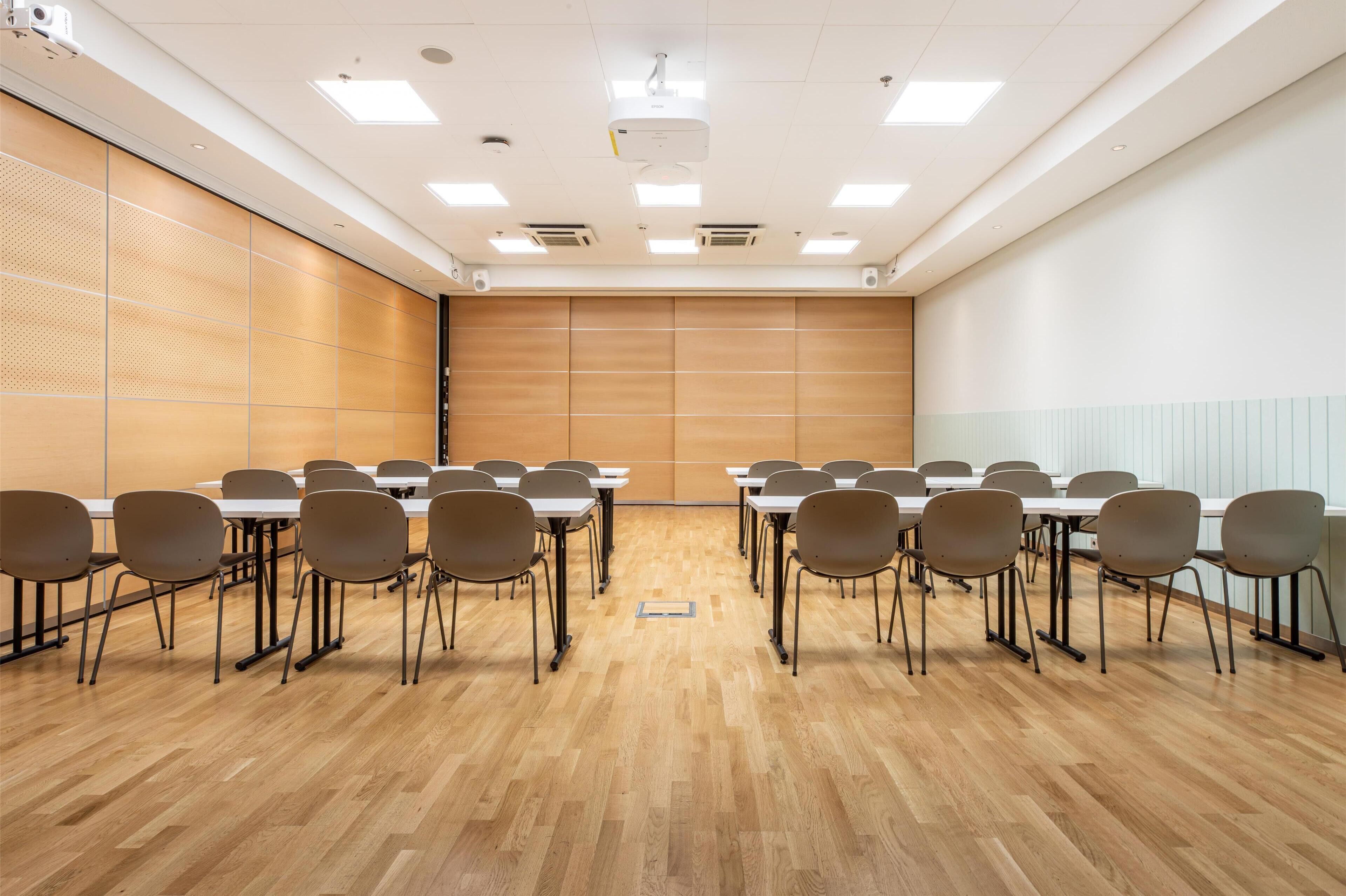 Un salón de conferencias con suelo de madera, paredes blancas y una pantalla de proyector grande.