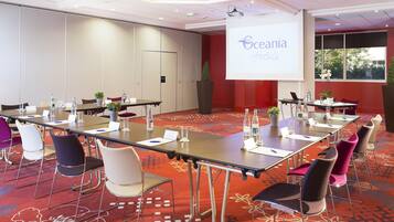 Een congreszaal met een groot scherm waarop het logo van Eceania Hotels staat, meerdere tafels met stoelen en een vloerbedekking.