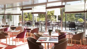 A modern restaurant with large windows, multiple tables and chairs, and a view of the outdoors.