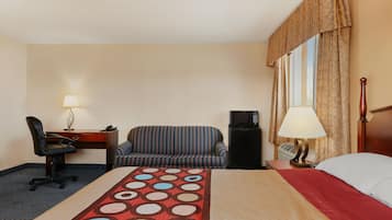 Une chambre d’hôtel comprenant un lit, un bureau avec une lampe, une chaise, un canapé, une télévision et une fenêtre avec des rideaux.