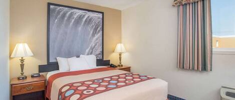 A hotel room with a bed, two bedside tables with lamps, a large framed picture on the wall, a window with curtains, and a tiled floor.