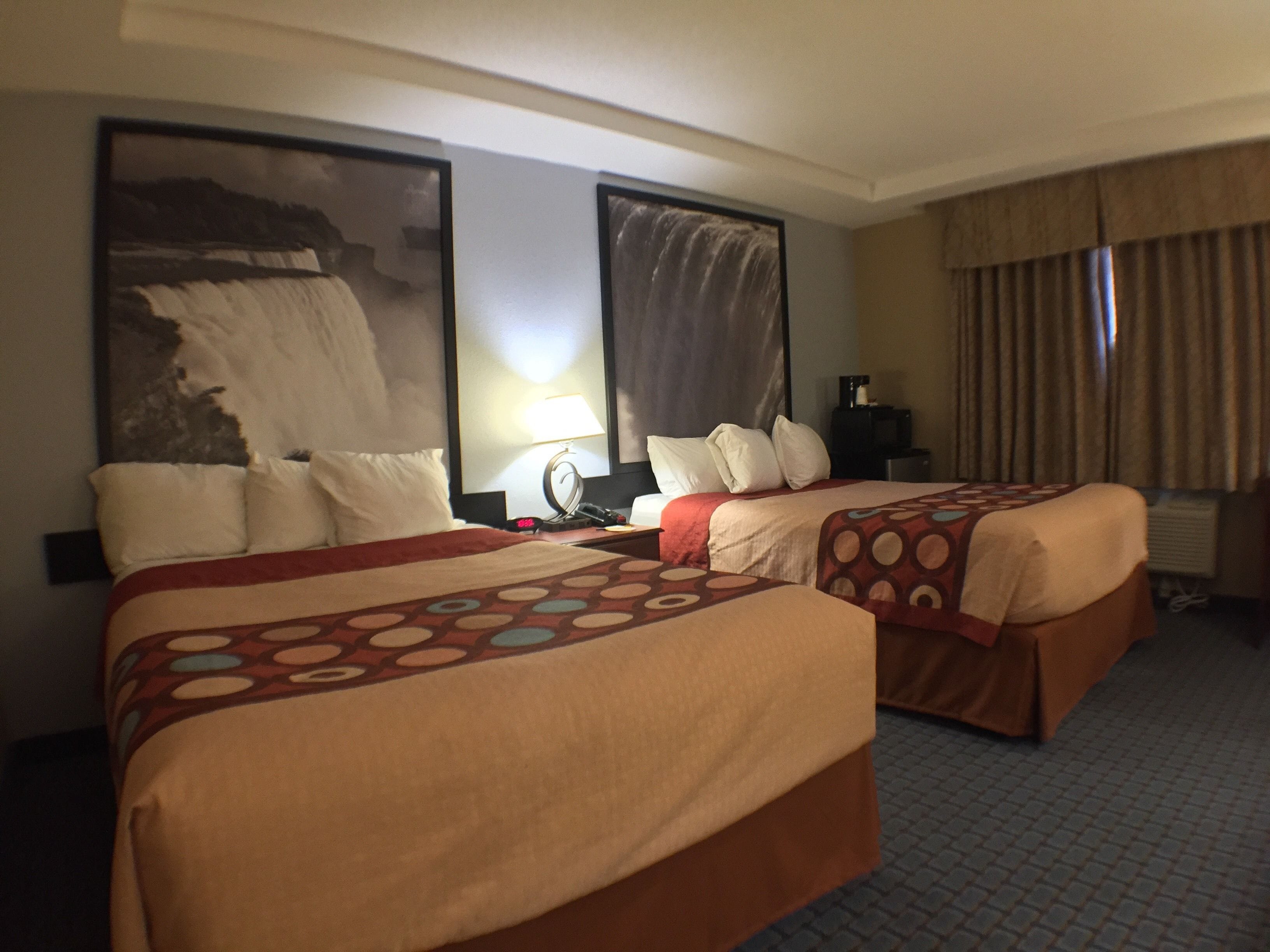 Habitación de hotel con dos camas, un cuadro grande en la pared, una lámpara y una ventana con cortinas.