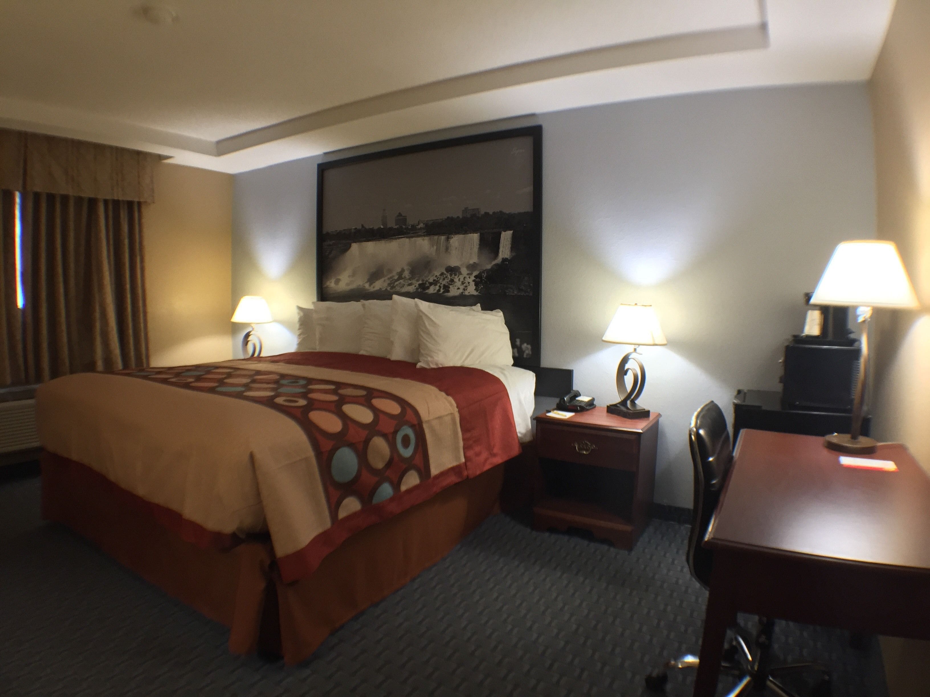 A hotel room with a large bed, two bedside tables with lamps, a desk, and a chair.