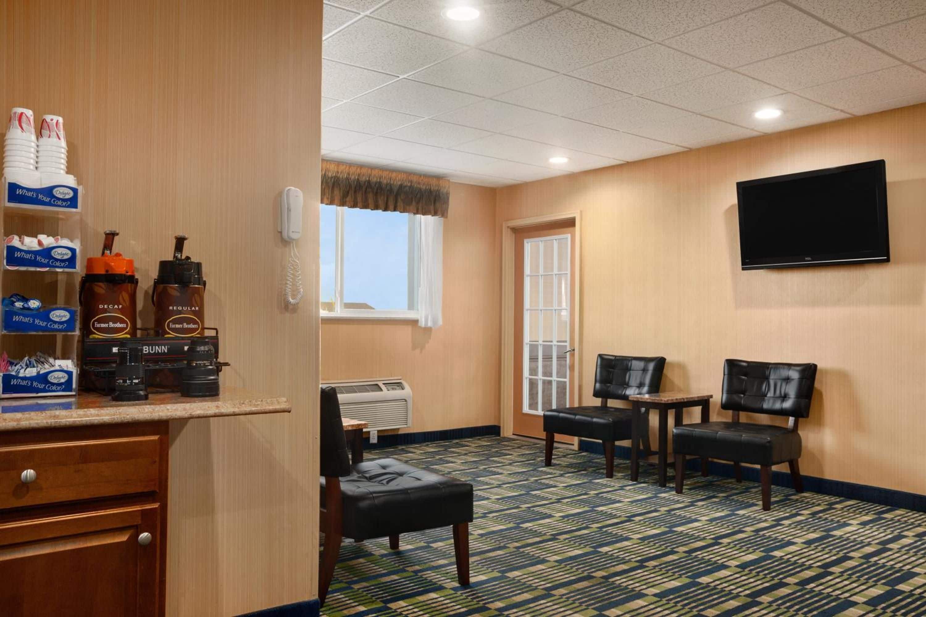 A hotel room with a kitchenette, a flat-screen TV mounted on the wall, a window with a view, and a patterned carpet.